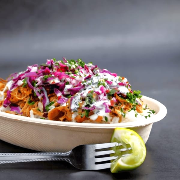 A Latin-American rice bowl with chicken, red cabbage, white sauce, and cilantro, with a lime wedge on a fork.